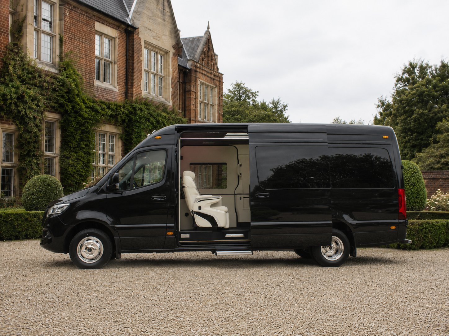 Black luxury van with open sliding door parked in front of ivy-covered brick manor house