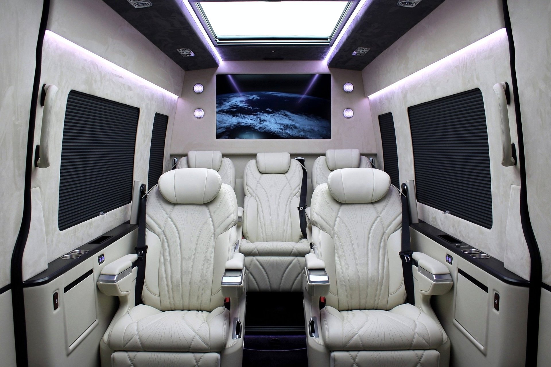 Luxury van interior with white leather seats, purple ambient lighting, a monitor displaying Earth, and panoramic sunroof