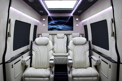 Luxury van interior with white leather seats, purple ambient lighting, a monitor displaying Earth, and panoramic sunroof