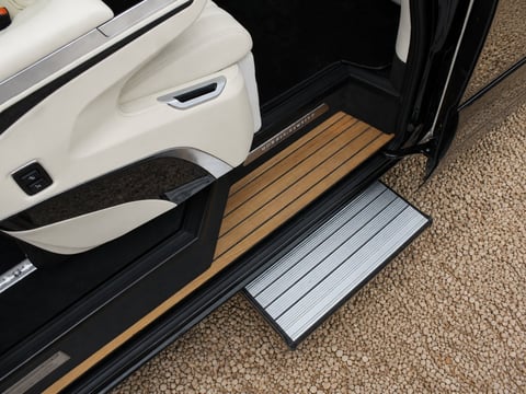 Open car door showing white interior panel and wooden step with aluminum sliding step extender on carpeted floor