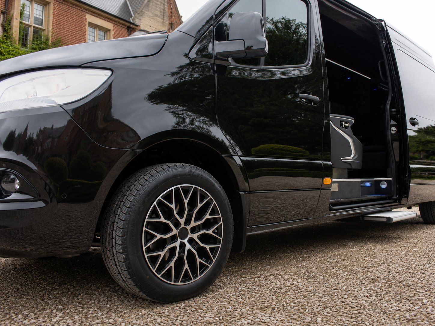 Black luxury van with open side door and decorative alloy wheels parked on driveway