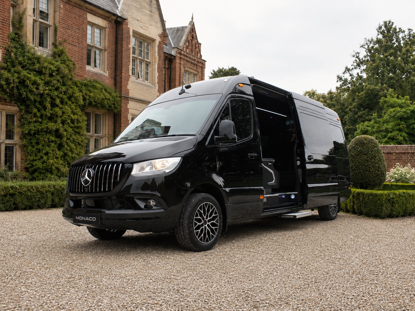 Black Mercedes-Benz van parked in front of a brick mansion with ivy and manicured hedges