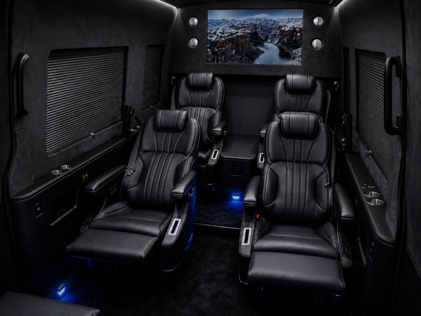 Luxury vehicle interior with four black leather seats, mounted monitor displaying mountain landscape, and ambient blue lighting