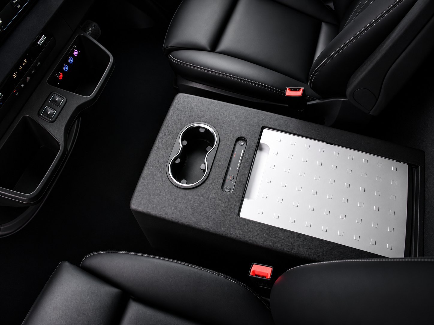 Car center console with wireless phone charger and white mat between black leather seats, red button visible