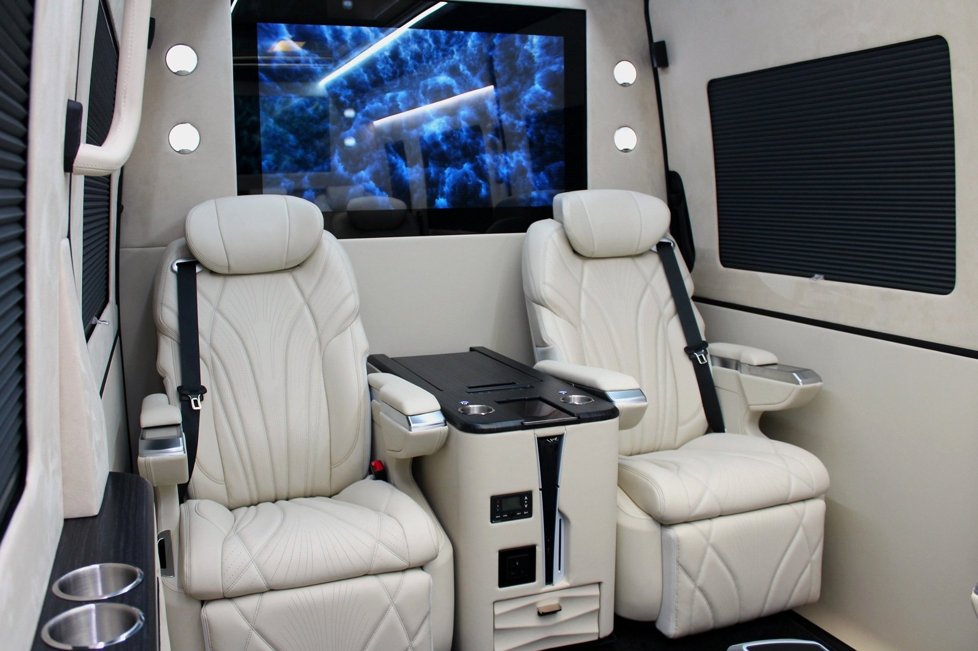 Interior of a luxury van with white leather captains seats, a mounted screen displaying blue graphics, and modern black accents