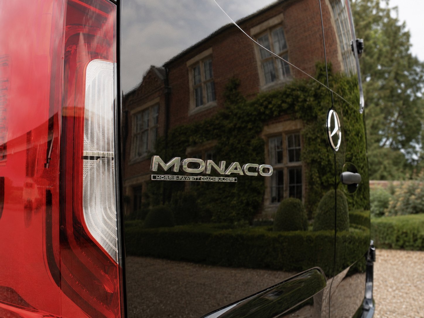 Red Monaco RV parked outside brick building with ivy and green surroundings