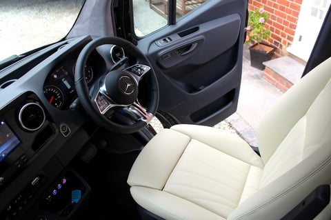 Interior of a convertible car with black steering wheel, white leather seat, and dashboard visible through open door