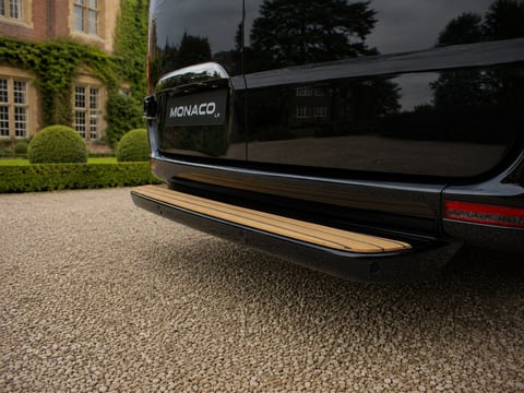 Rear view of black Monaco luxury vehicle parked on gravel driveway with ivy-covered building and manicured garden in background