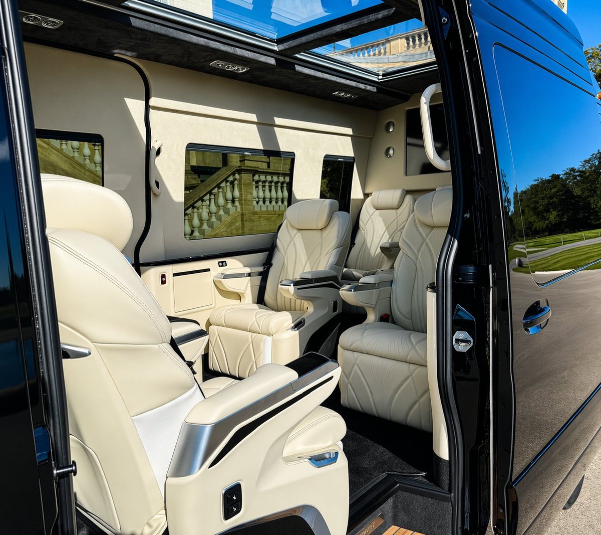 Interior of a luxury van with cream-colored leather seats, panoramic sunroof, and open door showing spacious seating arrangement