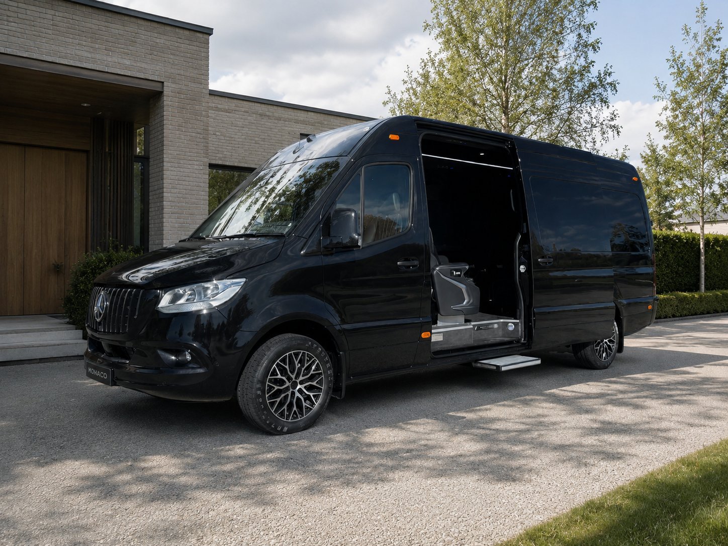 Black luxury van with open sliding door parked on driveway in front of modern house