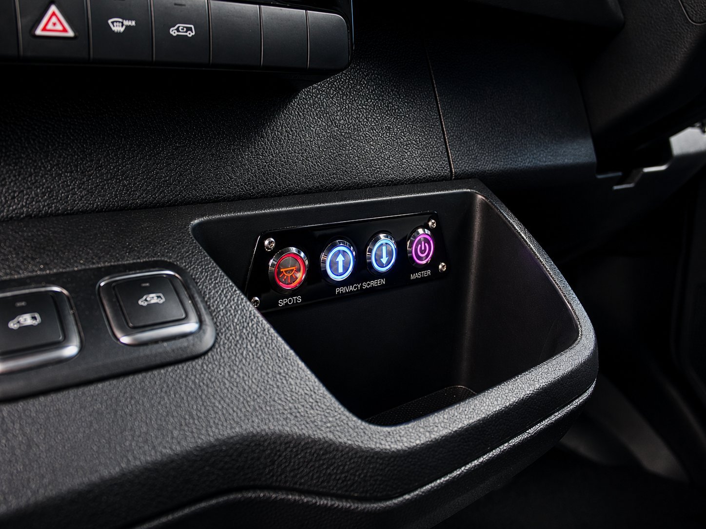 Car dashboard detail showing illuminated function buttons and indicator lights in a dark interior