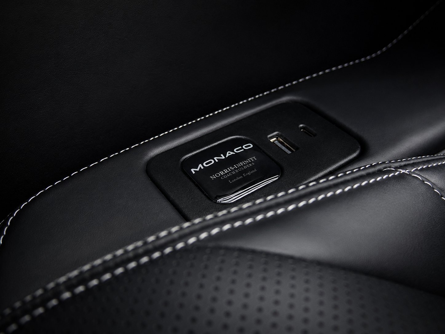 Close-up of black leather car interior with Monaco badge and white stitching detail
