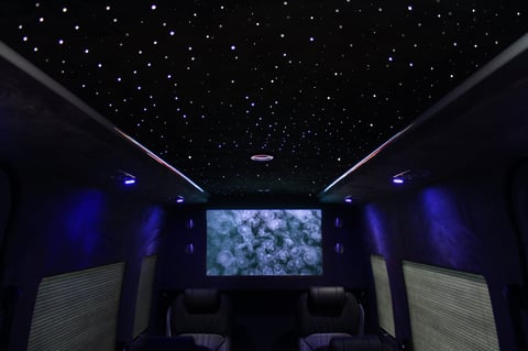 Modern home theater with starry ceiling, blue ambient lighting, wall speakers, and large center screen displaying celestial imagery