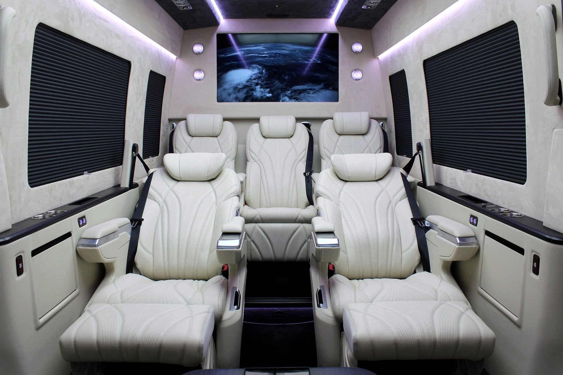Luxury van interior with cream leather seats, blue-tinted display screen, and modern ambient lighting throughout the cabin