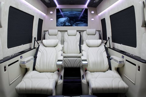 Luxury van interior with cream leather seats, blue-tinted display screen, and modern ambient lighting throughout the cabin