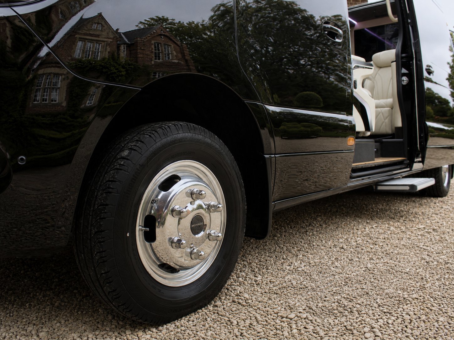 Close-up of a black luxury SUV with chrome wheel and open door, parked on a gravel driveway