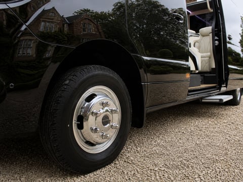 Close-up of a black luxury SUV with chrome wheel and open door, parked on a gravel driveway