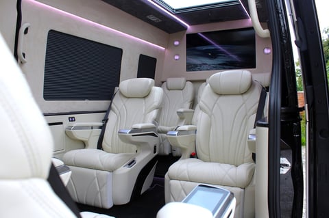 Luxury van interior with cream leather seats, ambient pink lighting, mounted TV screen, and modern cabin design